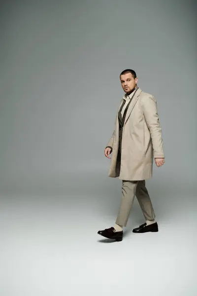 A man in a beige coat and trousers walks confidently in a studio. — Stock Photo