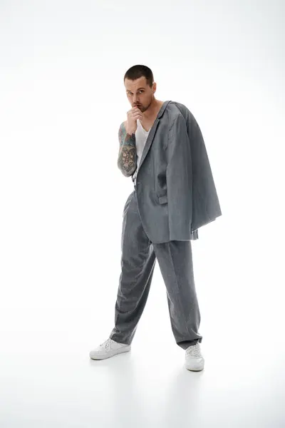 A stylish man in a grey suit with his jacket slung over his shoulder, stands thoughtfully. — Stock Photo
