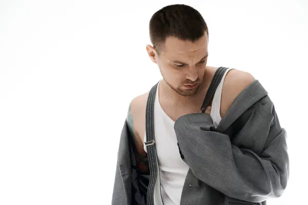 A man in a white undershirt and suspenders, adjusts his grey jacket. — Stock Photo