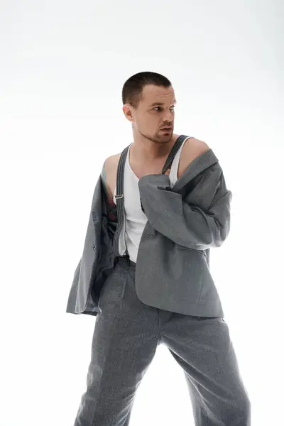 Ein Mann in grauer Anzughose und -jacke mit Hosenträgern blickt über die Schulter. — Stockfoto
