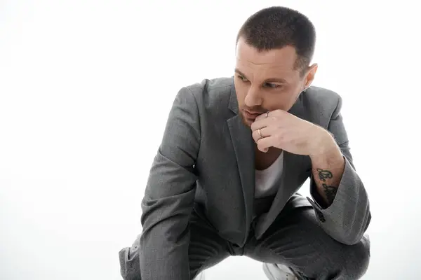 A stylishly dressed man in a grey suit kneels, thoughtfully resting his chin on his hand. — Stock Photo