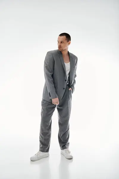 A man in a grey suit and white shoes stands against a white backdrop, looking over his shoulder. — Stock Photo