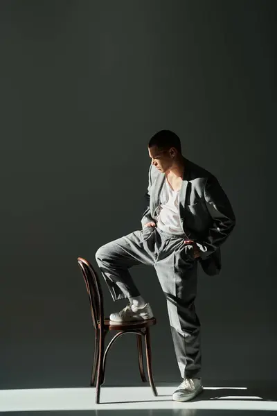 A stylish man in a gray suit stands with one foot on a chair, his other foot on the ground. — Stock Photo