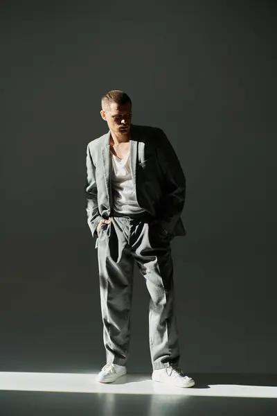 A stylish man in a grey suit poses against a grey backdrop, bathed in a single beam of light. — Stock Photo