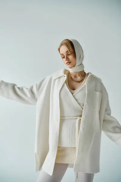 Una joven con un traje de punto blanco posa sobre un fondo azul claro. - foto de stock