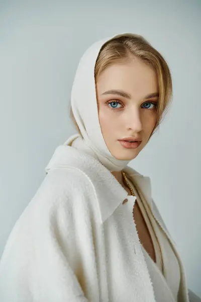 Uma jovem mulher com cabelo loiro usa um lenço branco e um casaco branco. — Fotografia de Stock