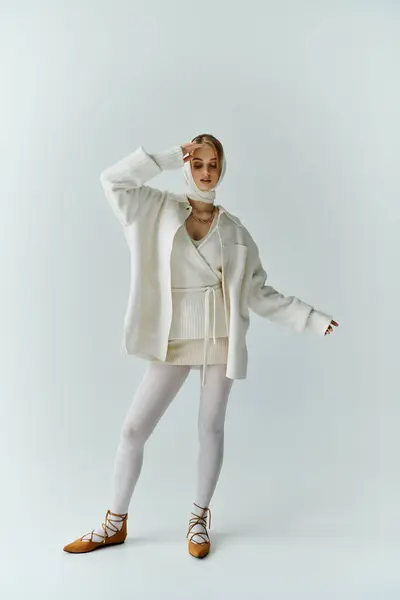 A young woman in a white outfit stands in a studio, her hand raised to her face. — Stock Photo