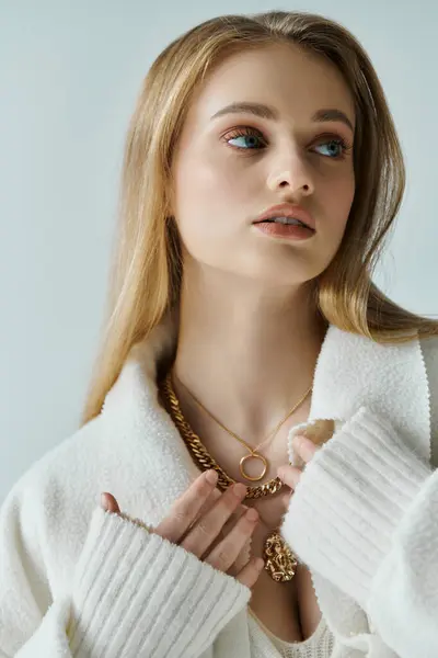 A young woman in a white sweater adjusts a golden necklace. — Stock Photo