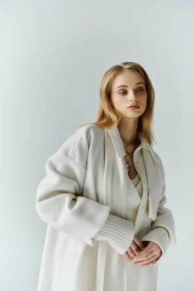 A young woman stands in a white coat, her gaze directed downwards. — Stock Photo