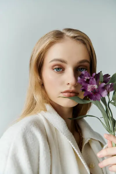 Una joven vestida con una túnica blanca mira fuera de cámara, sosteniendo flores moradas cerca de su rostro. - foto de stock