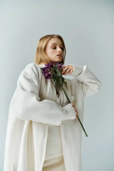 A young woman in a white cardigan holds a single sprig of purple flowers. — Stock Photo