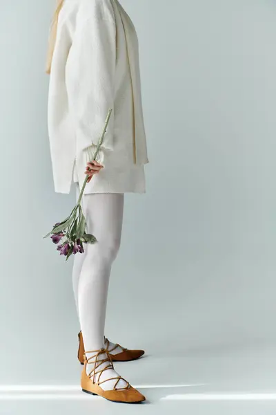 A young woman in white clothing poses with a bouquet of flowers in her hand. — Stock Photo