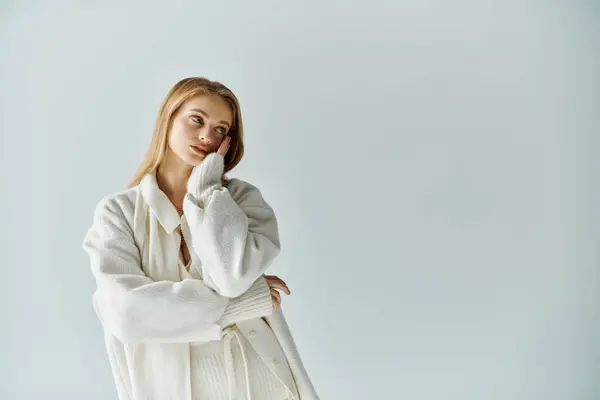 A young woman in a white cardigan contemplates against a soft, pale background. — Stock Photo