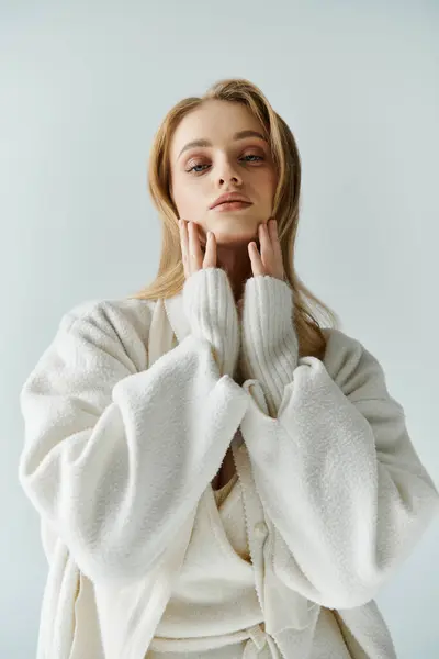 Eine junge Frau im weißen Pullover posiert zart, ihre Hände ruhen auf ihren Wangen.. — Stock Photo