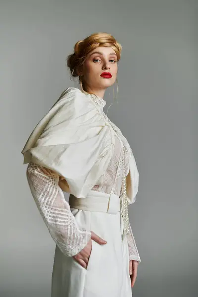 Young woman in white, stylish outfit stands against gray backdrop, hand in pocket. — Stock Photo