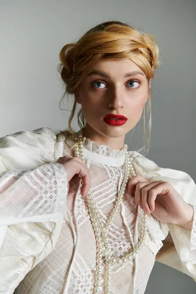 A young woman adjusts a pearl necklace while wearing an elegant white blouse. — Stock Photo
