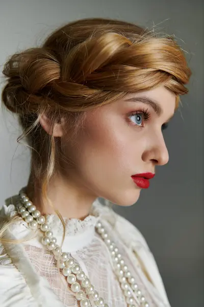 Una giovane donna con una collana di perle guarda a lato, i suoi capelli biondi in stile treccia. — Foto stock