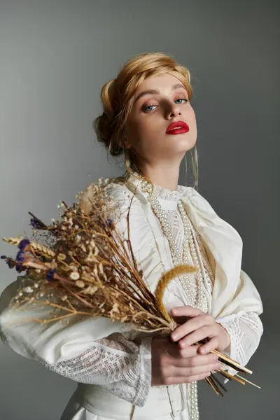 A young woman in a white, ruffled dress holds a bouquet of dried flowers. — Stock Photo
