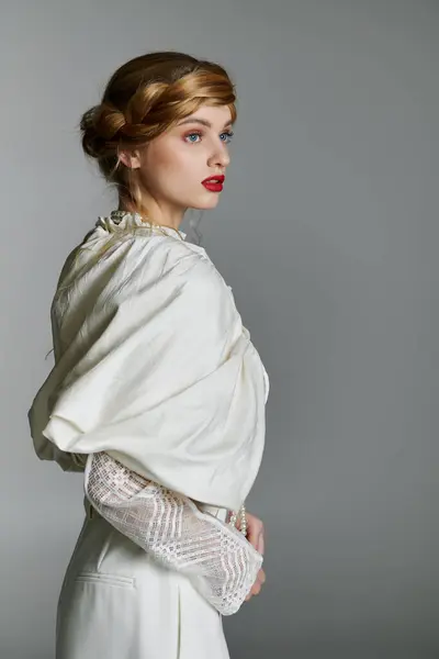 A young woman in elegant white attire stands against a gray backdrop, her gaze directed to the side. — Stock Photo