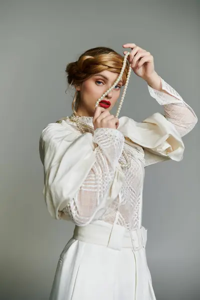 Женщина в белом кружевном топе и в брюках позирует с жемчужным ожерельем на лице. — стоковое фото