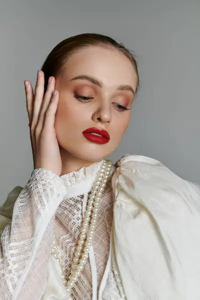 A young woman in a white lace blouse with pearl necklace thoughtfully rests her hand on her cheek. — Stock Photo