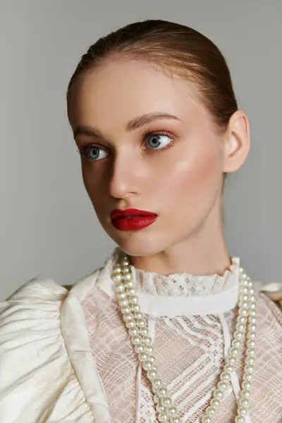A young woman with bright eyes and red lipstick wears a white lace blouse and pearl necklace. — Stock Photo