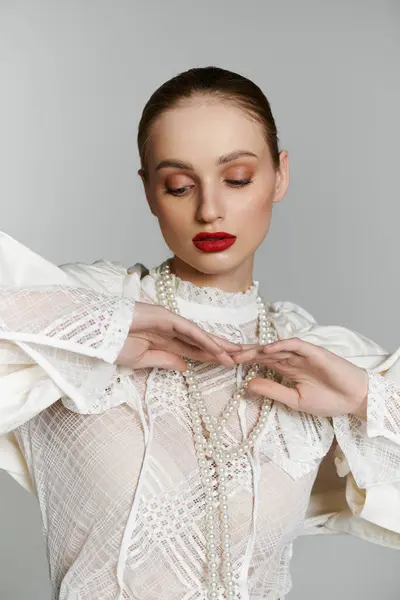 Young woman in white blouse adjusts pearl necklace, gazing down in contemplation. — Stock Photo