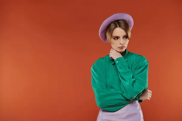 A woman in a lavender beret and green shirt poses against a vibrant orange backdrop. — Stock Photo