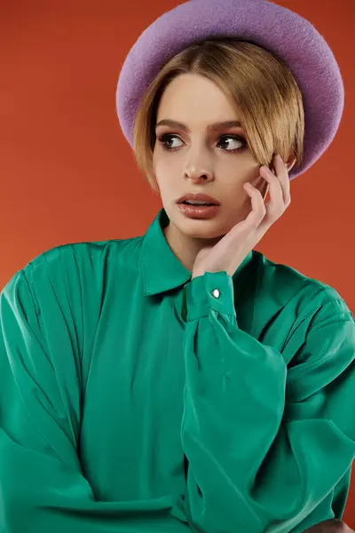 A young woman wearing a green shirt and lavender hat poses against a red background. — Stock Photo