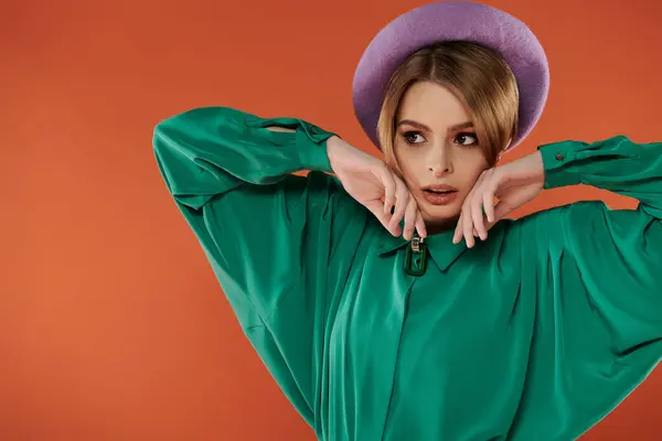 Stylish woman in green shirt and purple beret confidently poses on orange background. — Stock Photo