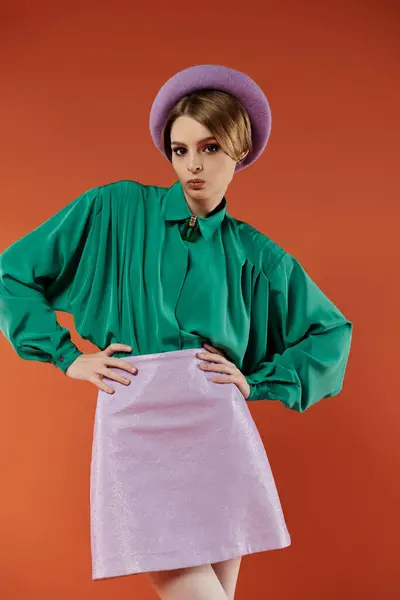 A young woman in a green blouse and lavender skirt poses against a bright orange backdrop. — Stock Photo