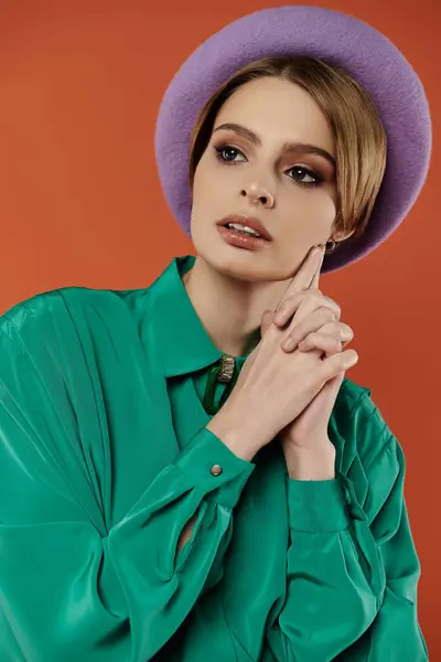 Stylish woman in purple beret and green shirt confidently poses against orange backdrop. — Stock Photo
