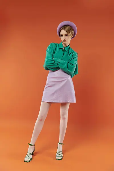 A woman in a lavender skirt and green blouse poses confidently against an orange backdrop. — Stock Photo