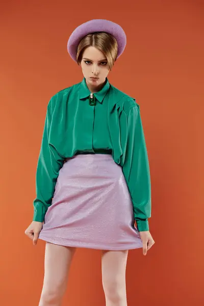 A woman in a green shirt and lavender skirt poses against a vibrant orange background. — Stock Photo