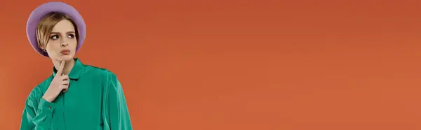 A woman in a green blouse and lilac beret ponders against an orange background. — Stock Photo