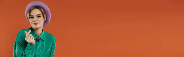A woman in a green shirt and purple beret poses confidently against a bright orange background. — Stock Photo