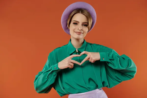 A stylish woman in a green shirt and purple beret makes a heart shape with her hands. — Stock Photo