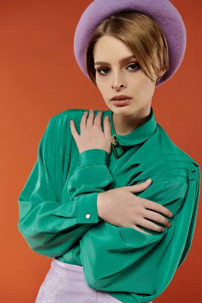 A woman in a vibrant green shirt and a lavender beret poses against a warm orange backdrop. — Stock Photo