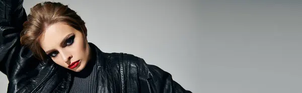 A woman in a black leather jacket poses against a grey backdrop. — Stock Photo