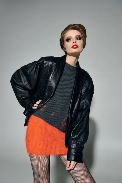 Stylish woman in leather jacket and orange skirt against grey background. — Stock Photo