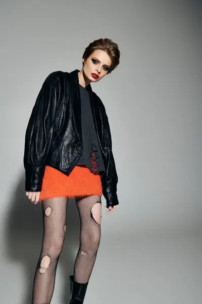 Woman with short hair in leather jacket, orange skirt, and fishnet tights, posing. — Stock Photo