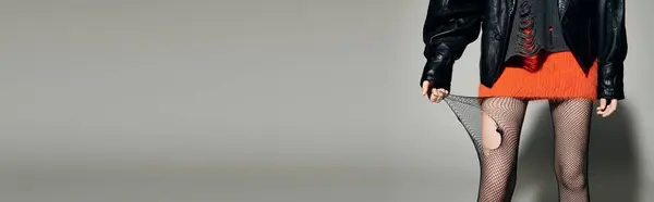 A woman in a leather jacket and a short, orange skirt adjusts her fishnet tights. — Stock Photo