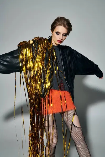 A stylish woman in a black leather jacket poses with a cascade of golden streamers. — Stock Photo