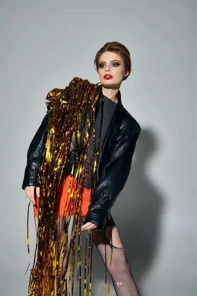 Confident young woman poses against plain backdrop with golden tinsel. — Stock Photo