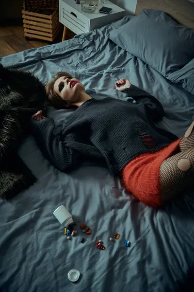 A stylish woman lies on a bed, surrounded by scattered pills and an overturned bottle. — Stock Photo