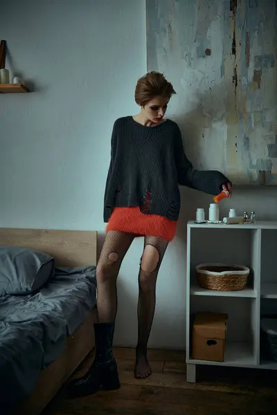 A woman in a red skirt and fishnet stockings poses by a bed in a stylish, grungy setting. — Stock Photo