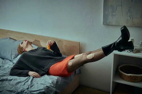 A young woman in a chic grungy style lies on a bed, legs raised, with a relaxed expression. — Stock Photo