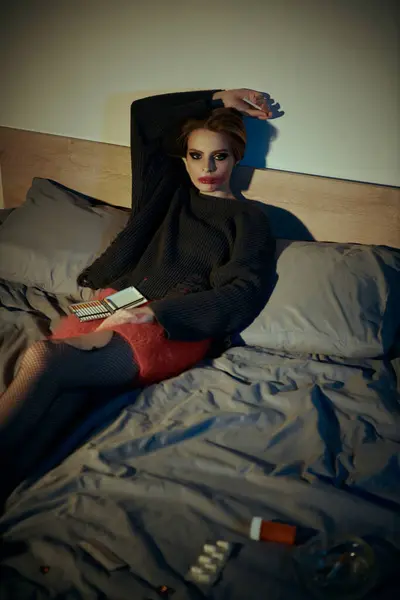 Woman in black sweater and red skirt poses casually on a bed with a stylish edge. — Stock Photo