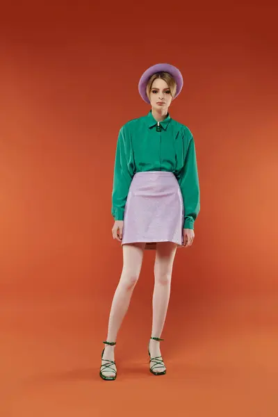 A woman in a green shirt and a lavender skirt poses against an orange background. — Stock Photo