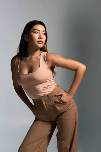A woman in a pink tank top and brown pants poses confidently in a studio setting. — Stock Photo